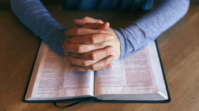 Mies rukoilemassa kädet ristissä ja Raamatun päällä